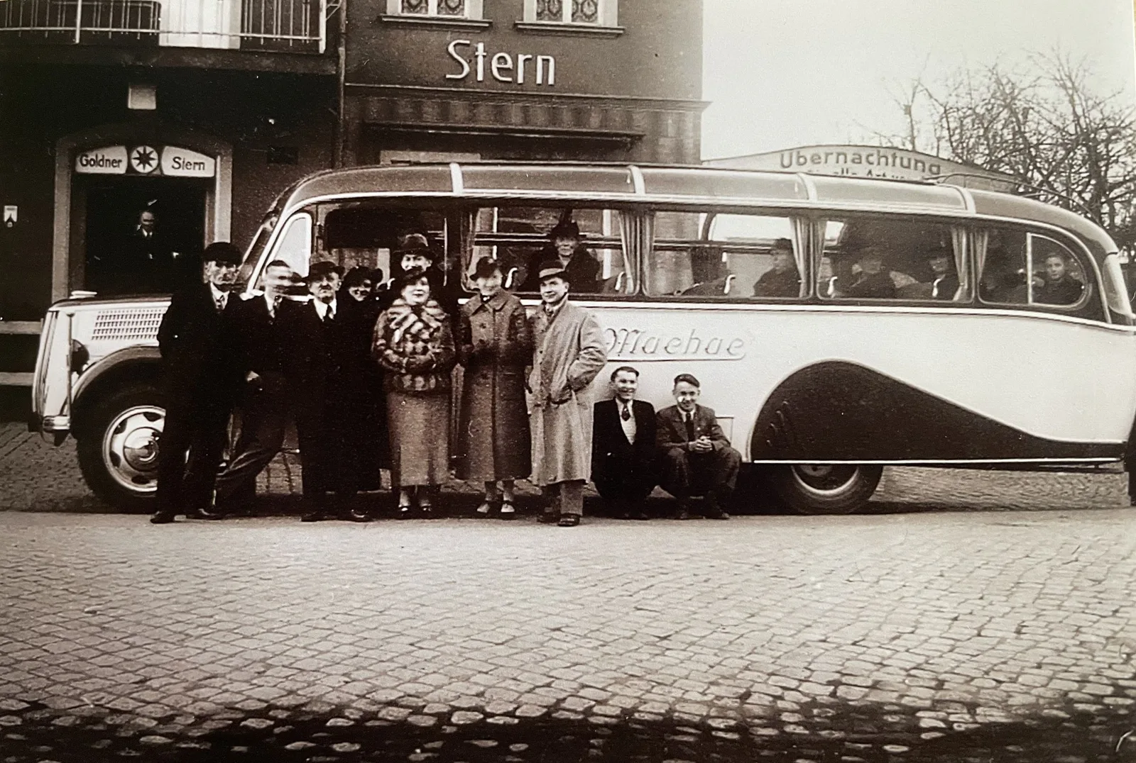 A 1930s Machac motor coach outside the Goldner Stern inn, its passengers and crew lined up along the cobbles for the photograph.